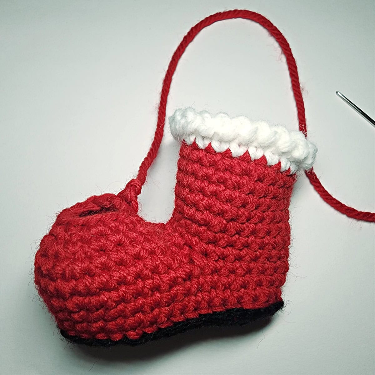 Small crochet Santa boot with toe opened and being closed with yarn needle.