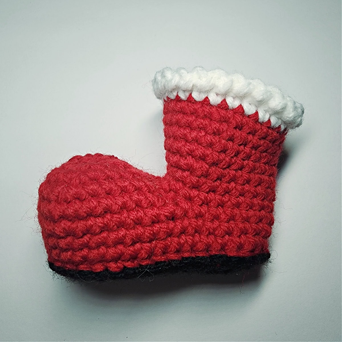 Plain red Santa boot ornament laying on white background.