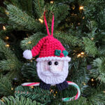 Santa Crochet Candy Cane Ornament hanging on a tree holding a candy cane.