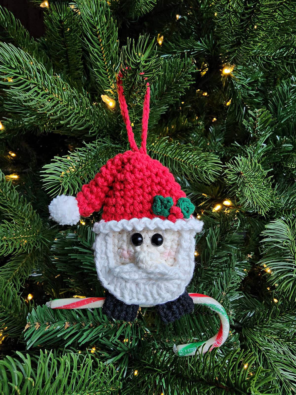 Handmade crochet Santa ornament holding a candy cane hanging on a Christmas tree.