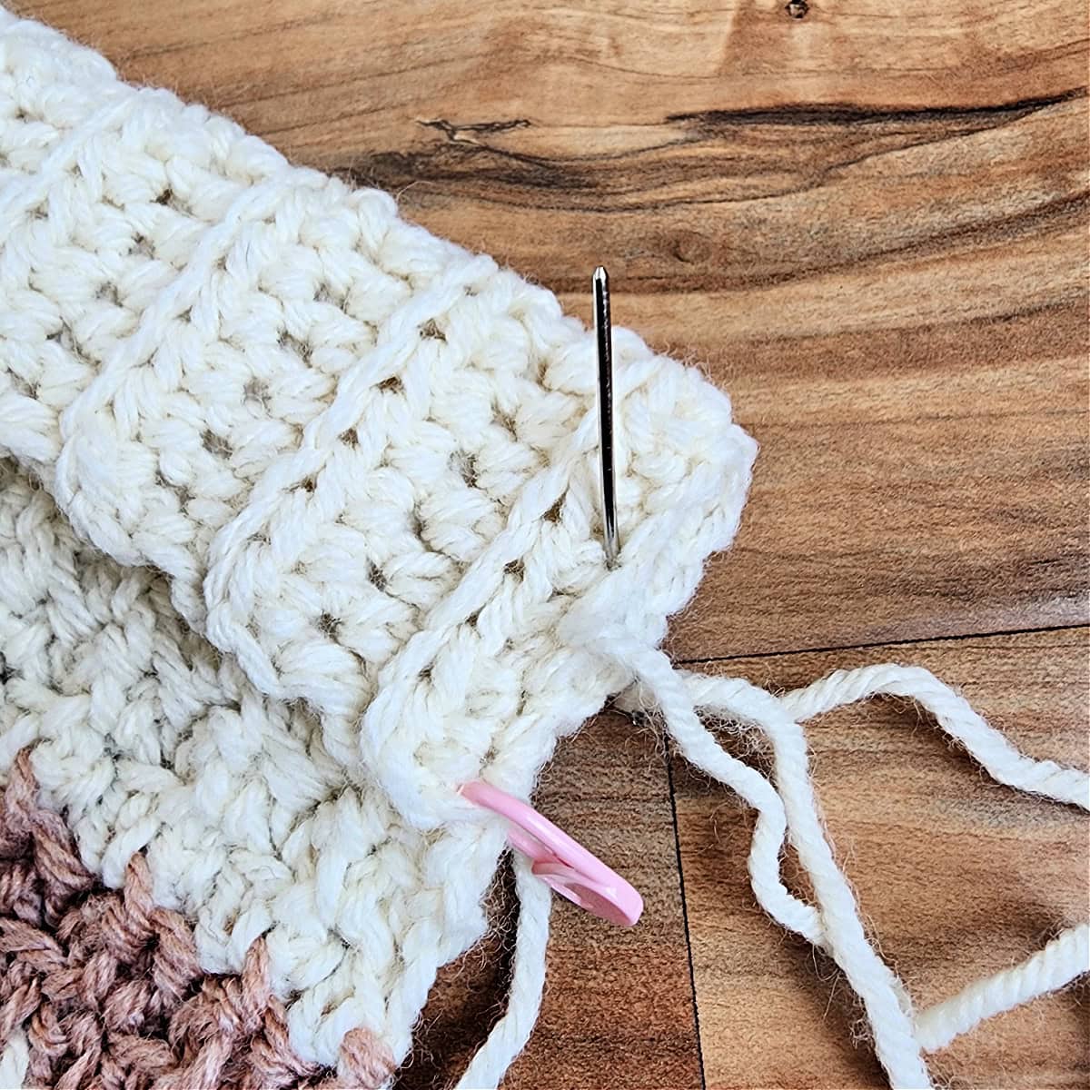 Close-up of a yarn needle whipstitching the edges of pocket ribbing together on a pocket scarf.