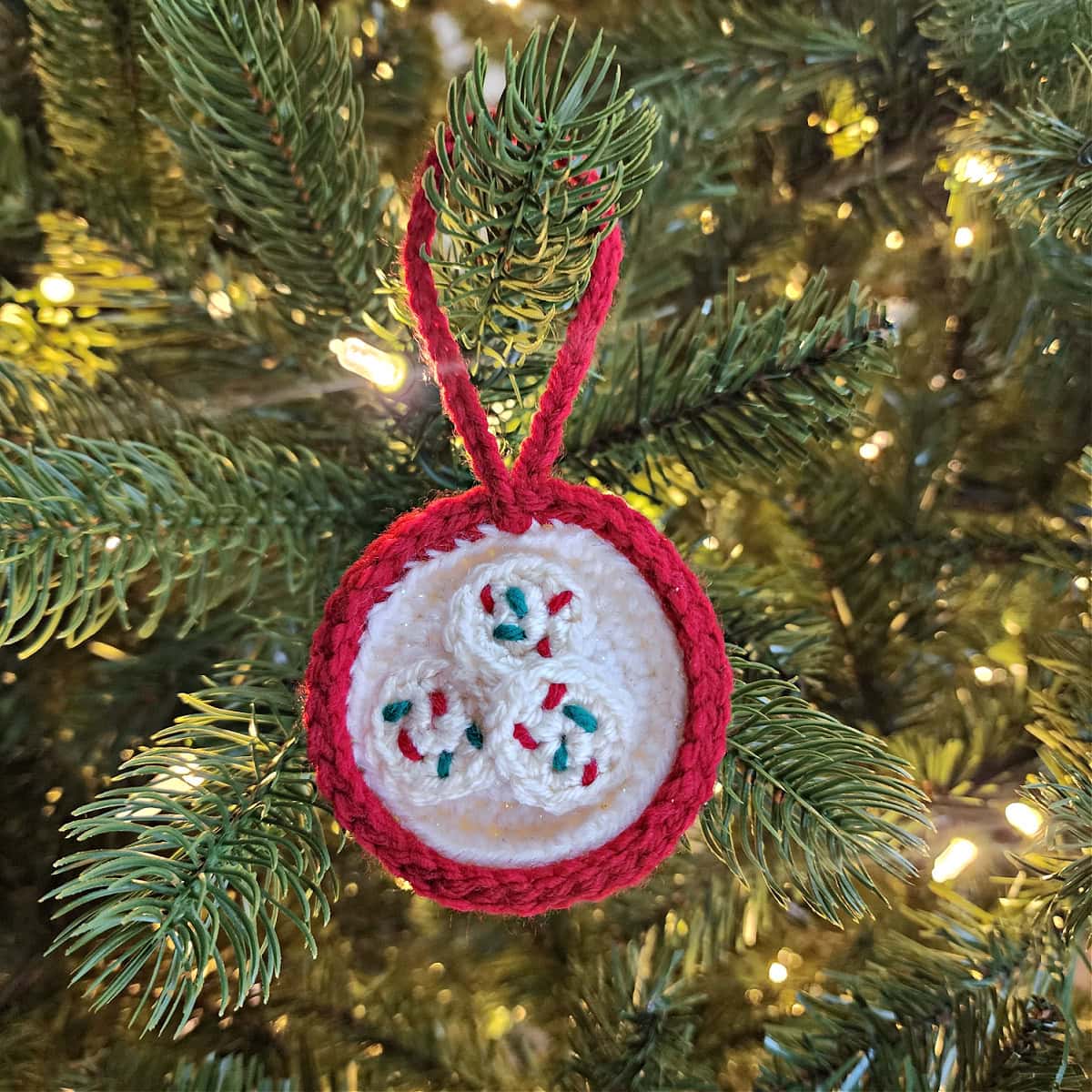 Crochet plate of cookies for Santa ornament hanging on a tree with white lights.