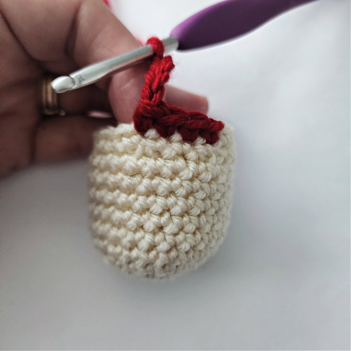 Crochet hook with red yarn showing how to add an arm onto the amigurumi head.