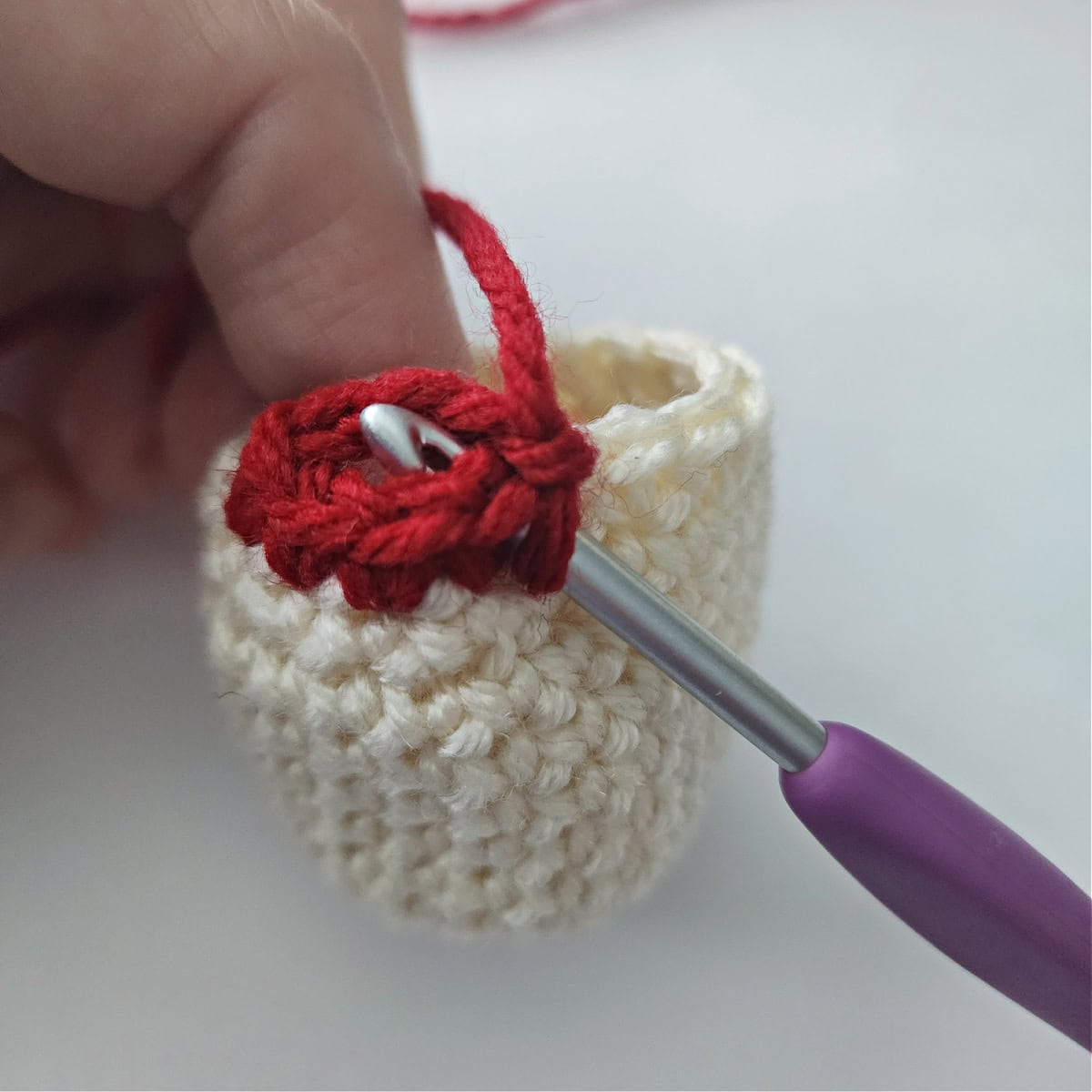 Purple crochet hook with red yarn forming a loop to crochet an arm on a crochet ornament.