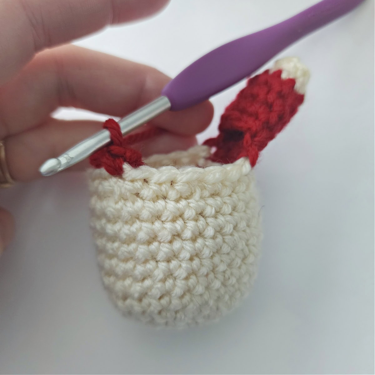 A crochet hook and red yarn starting to add the second arm on the amigurumi head.