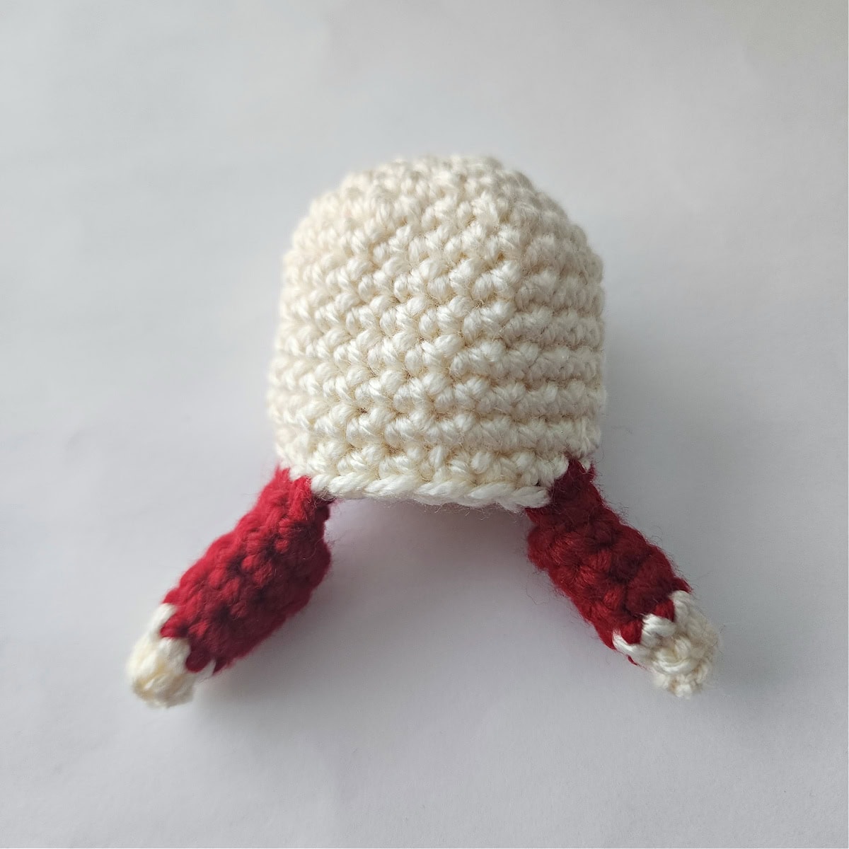 The head of a crochet jingle bell ornament with both arms complete.