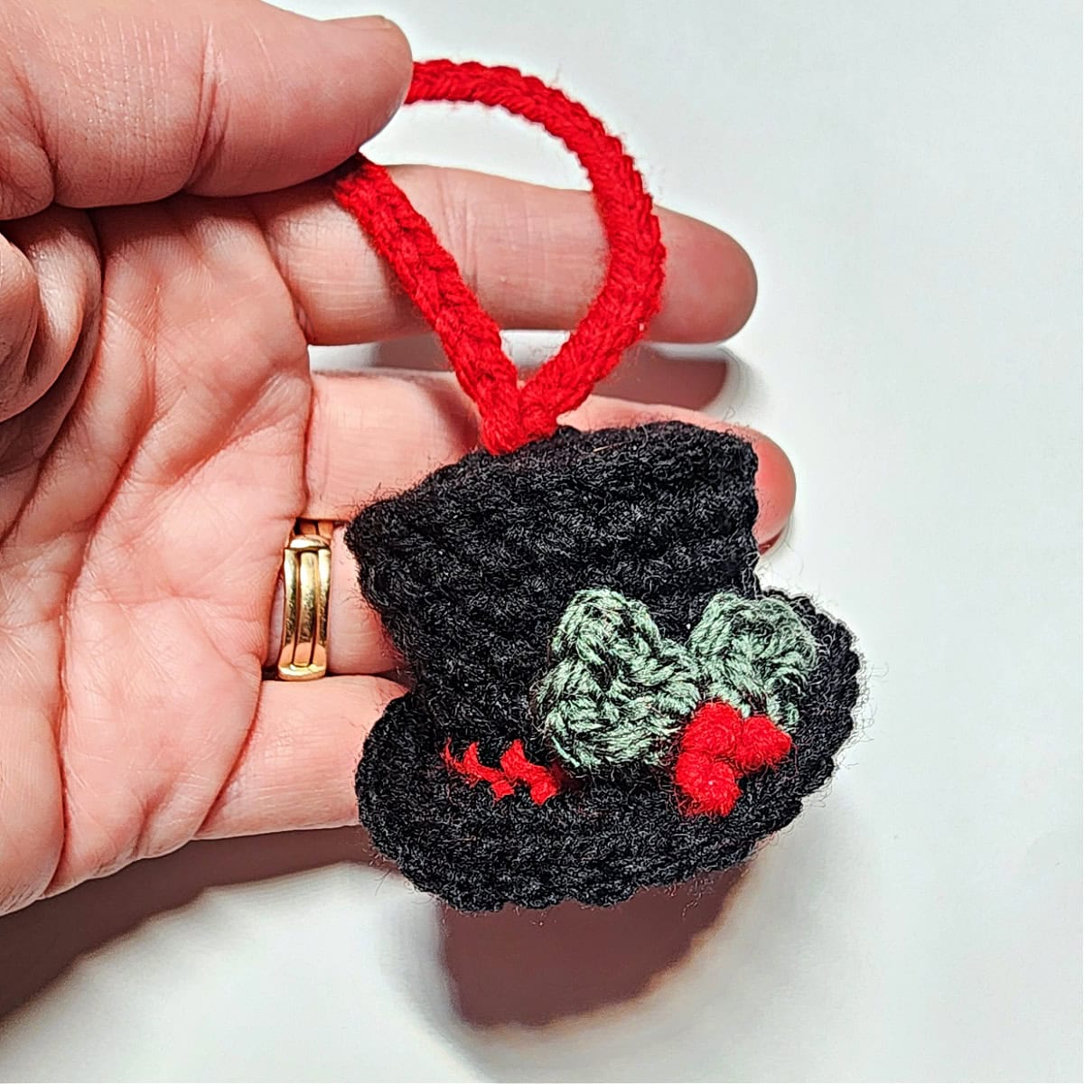 Hand holding small crochet snowman hat with holly leaves and berries.