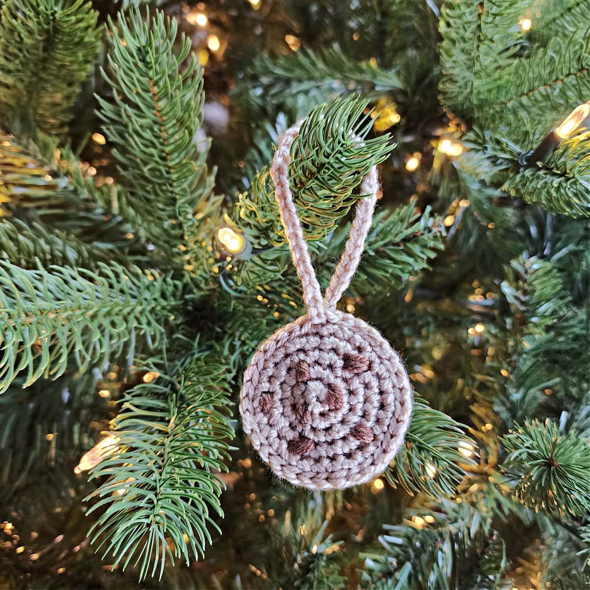 Chocolate chip crochet cookie ornament hanging on a Christmas tree.