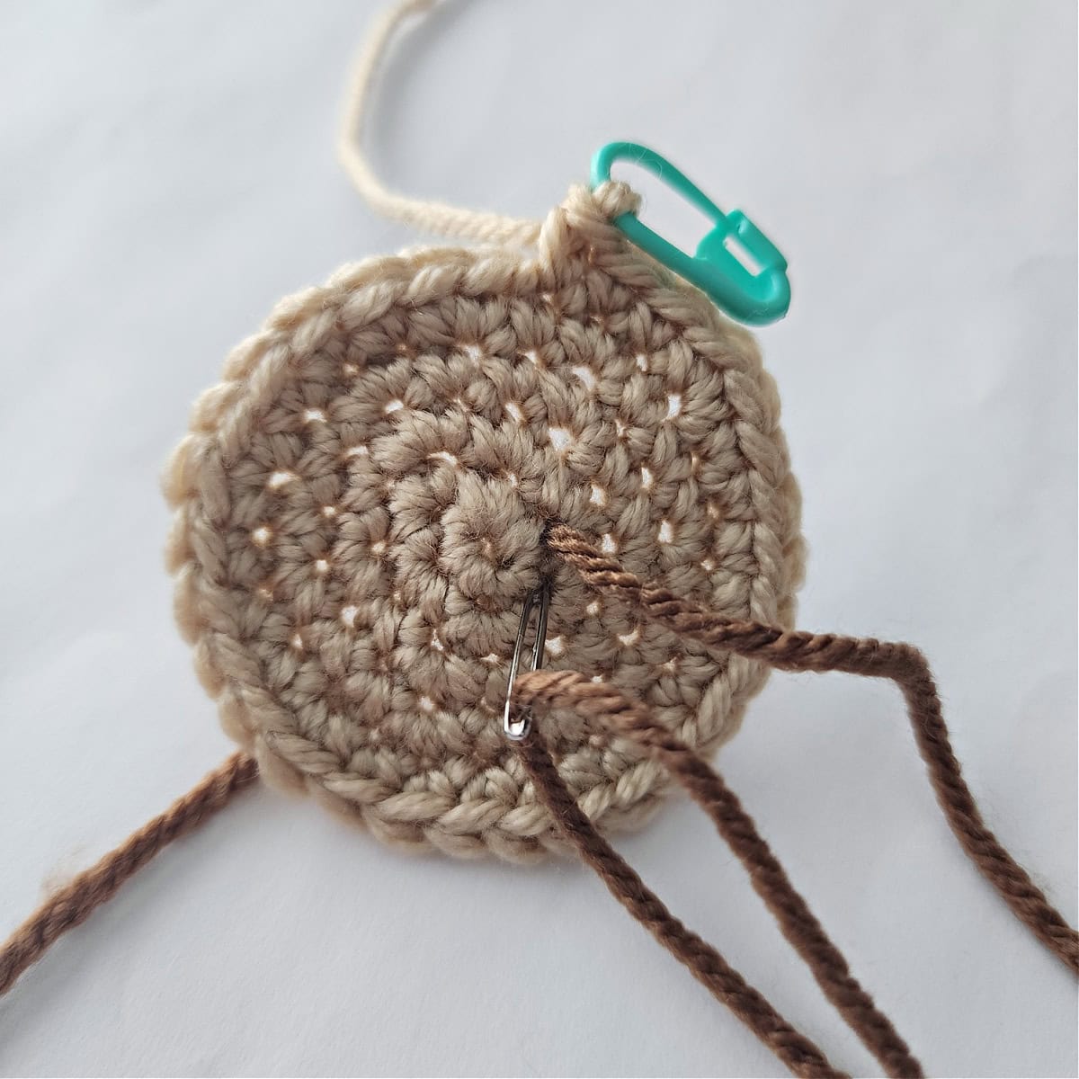 A yarn needle and dark brown yarn adding chocolate chips to a crochet cookie.