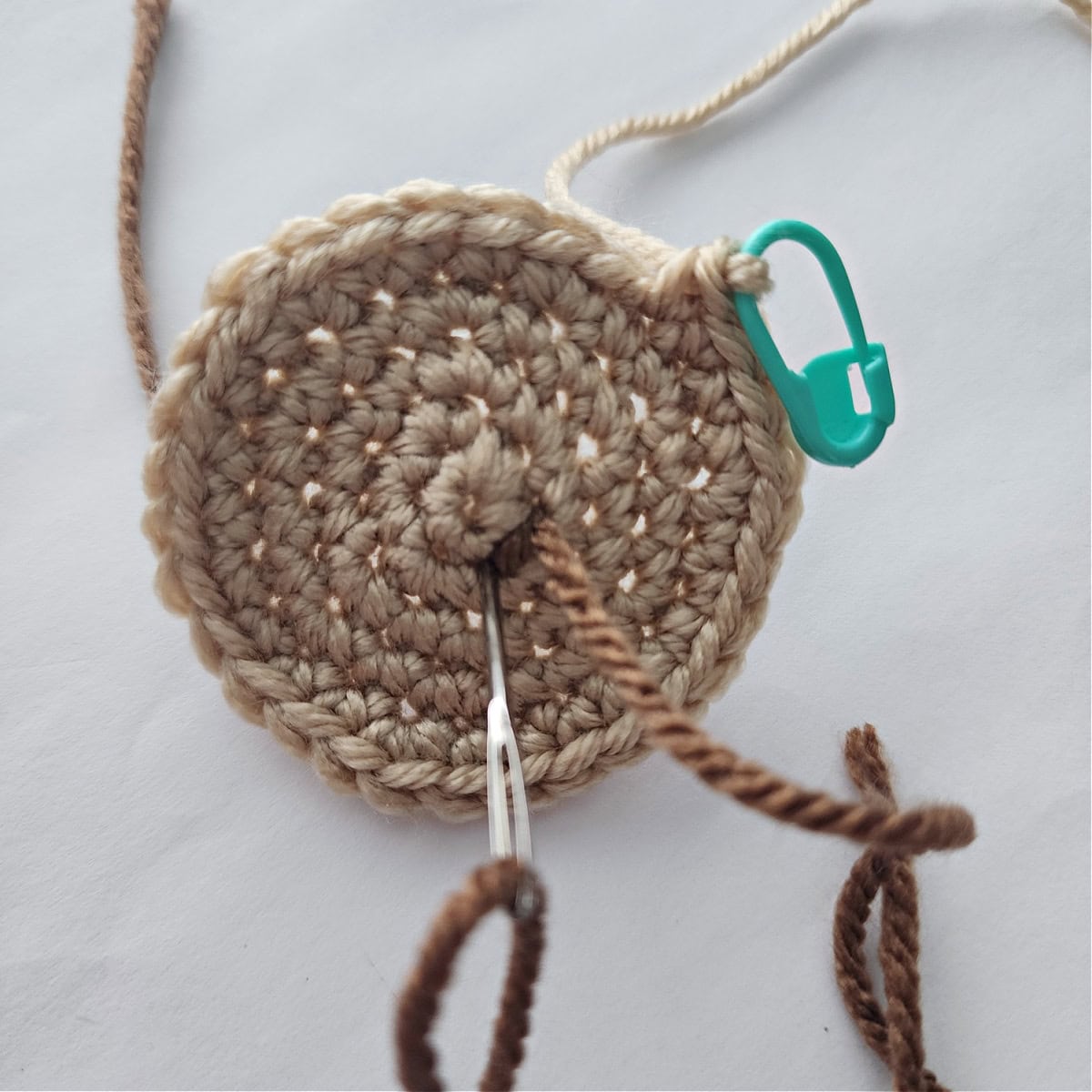 Dark brown yarn being embroidered on a crochet cookie to look like chocolate chips.