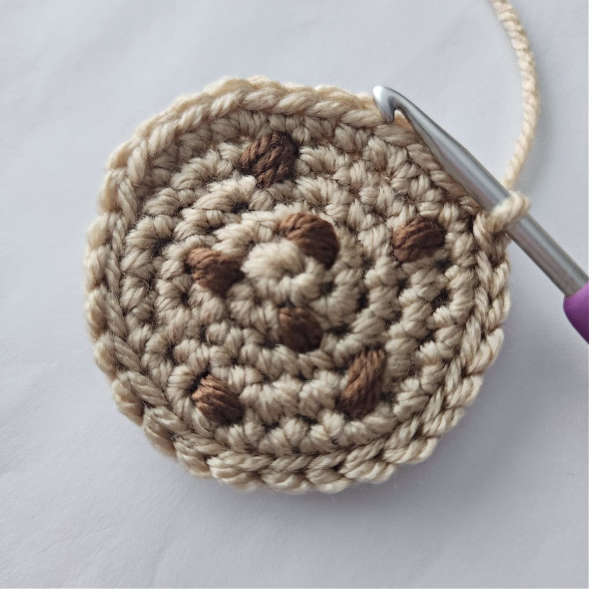 Right side of a chocolate chip crochet cookie being slip stitched to a plain brown circle.