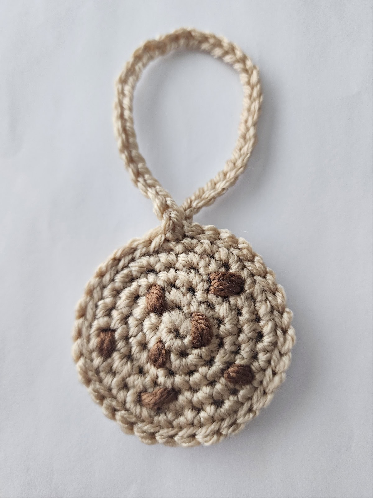 A crochet chocolate chip cookie ornament laying on a white surface.