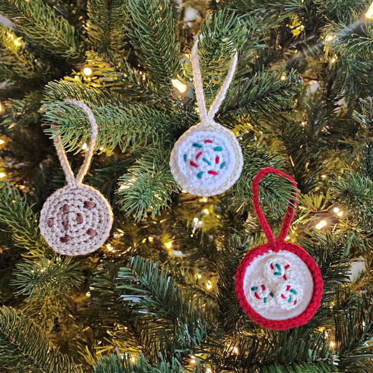 Three crochet Christmas cookie ornaments hanging on a lit tree.