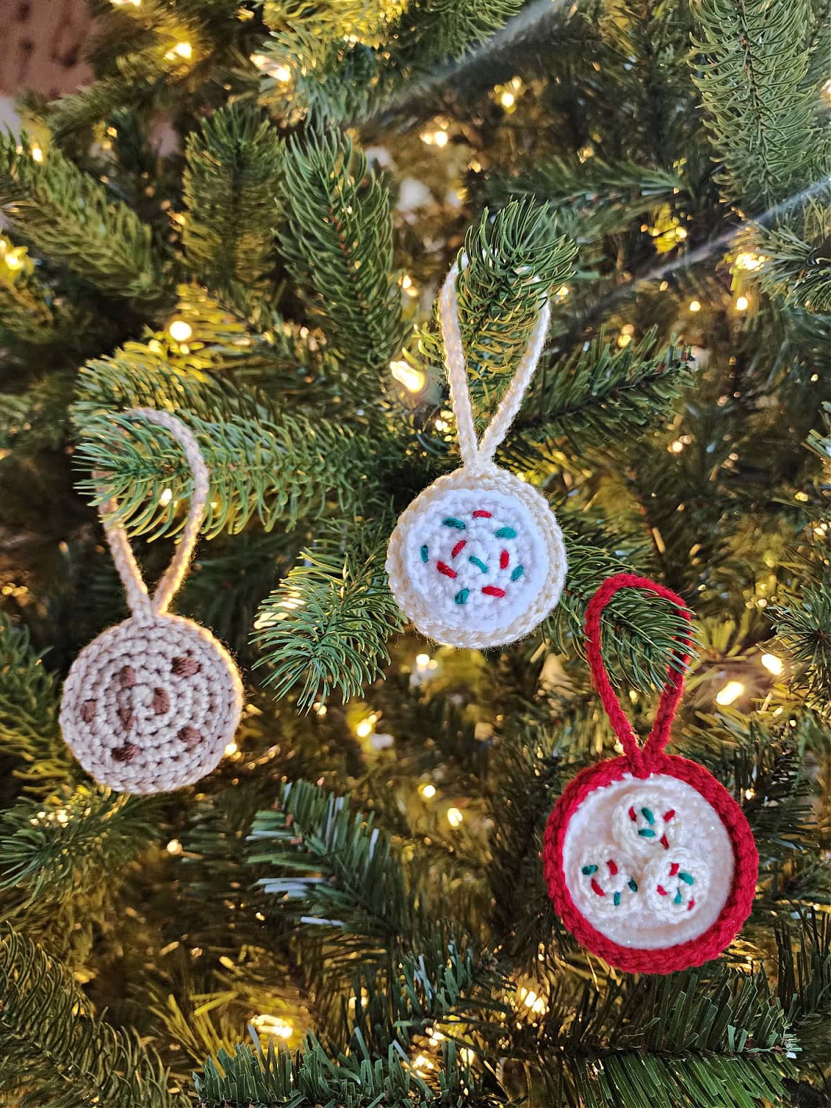 Crochet Christmas ornaments hanging on a Christmas tree with white lights.