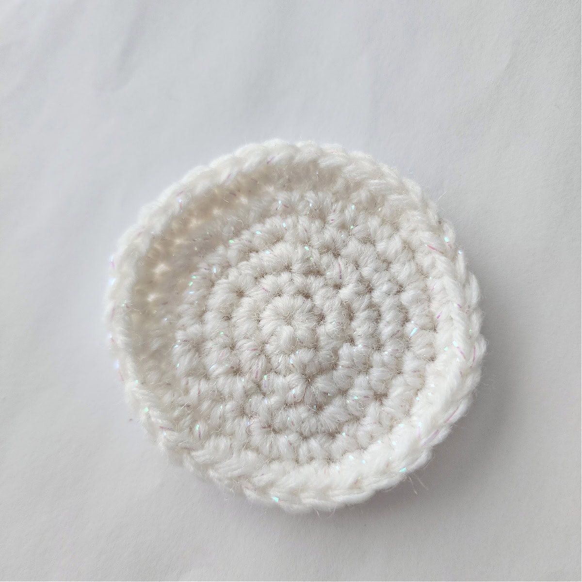 A circle crocheted using white yarn with iridescent strands throughout.