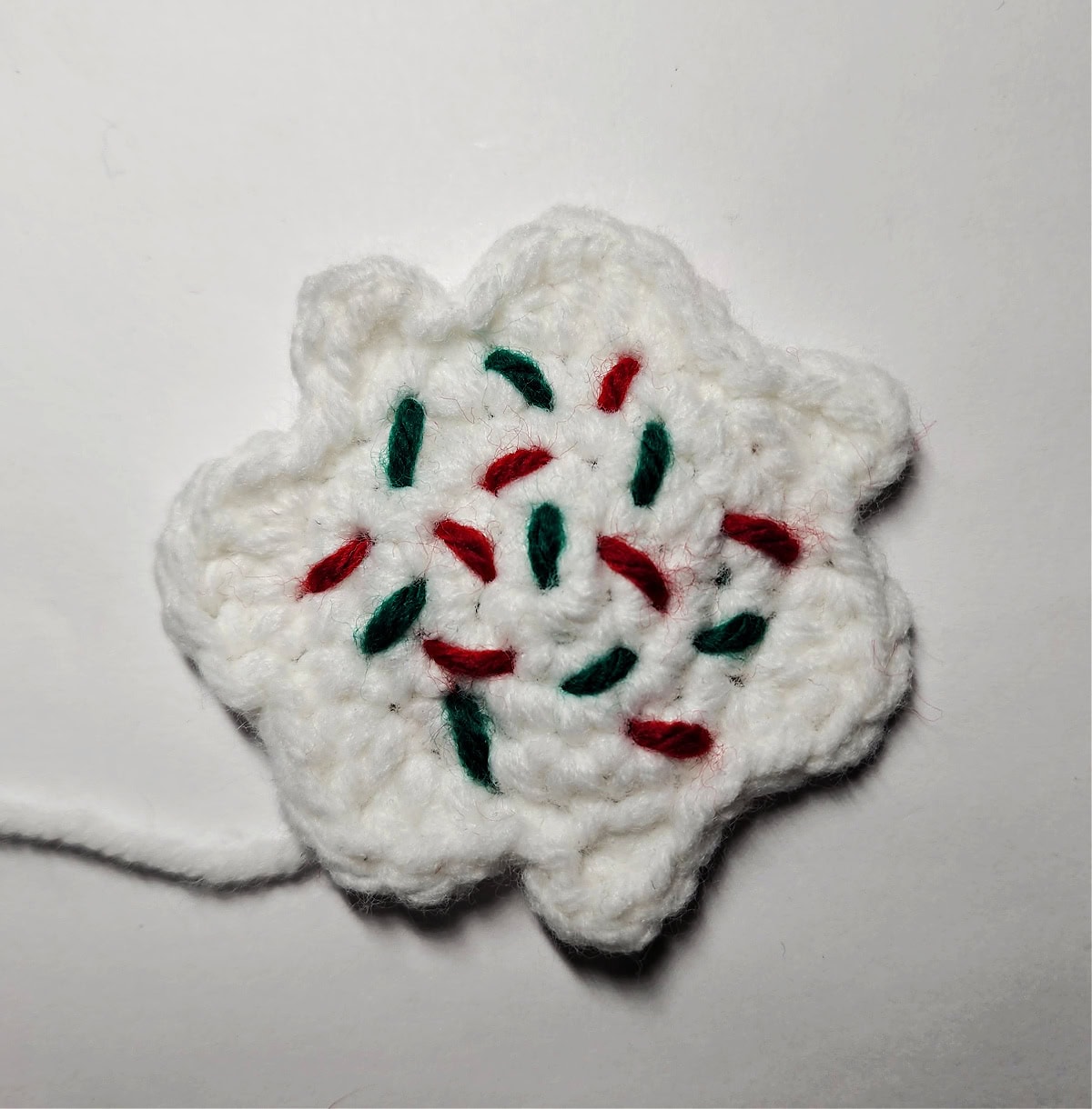 White crochet abstract shape for icing hair on gingerbread girl with red and green sprinkles.