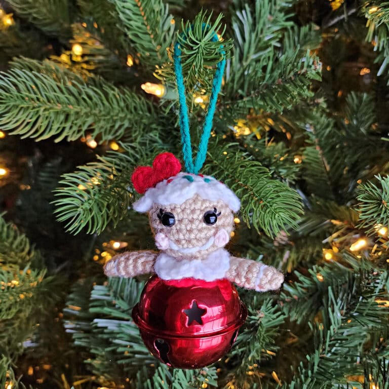 Crochet gingerbread girl jingle bell ornament hanging on a Christmas tree.