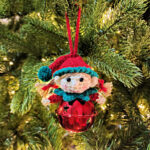 A sweet little girl elf crochet Christmas ornament hanging on a Christmas tree.