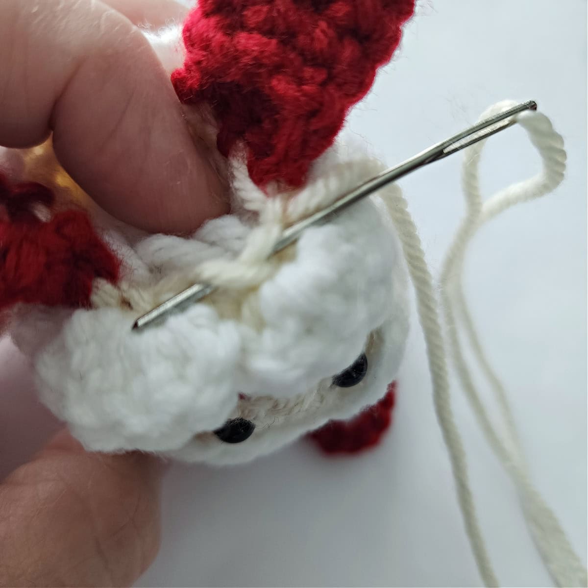 A yarn needle and tail of yarn weaving in and out of crochet circle to close the head.