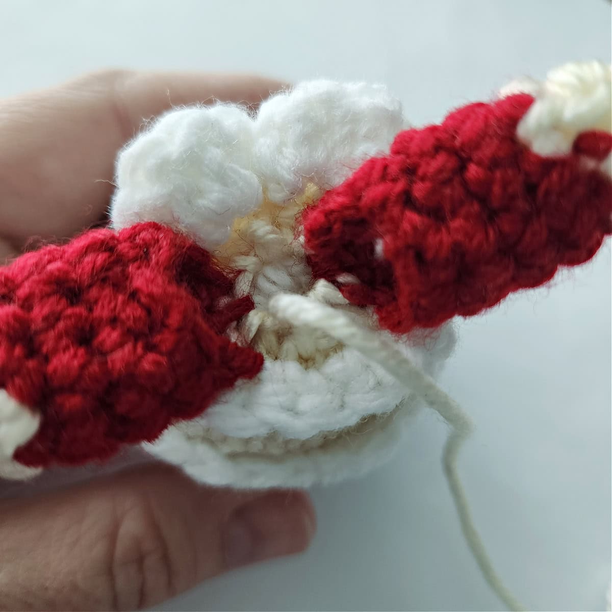 A yarn tail pulled tight to cinch the crochet amigurumi head closed.