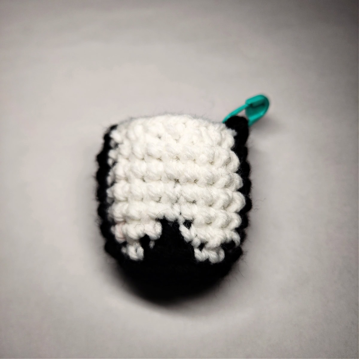 A crochet penguin head laying upside down with a green stitch marker.