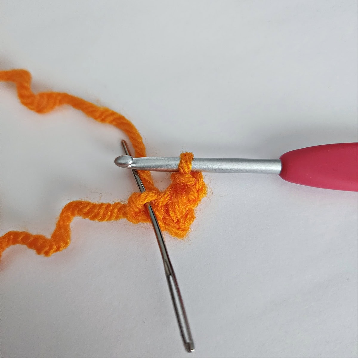 Orange yarn with crochet hook and yarn needle to crochet a beak.