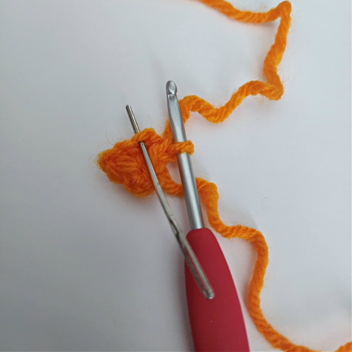 Tutorial photo with a crochet hook and yarn needle to show how to crochet a beak for a penguin.