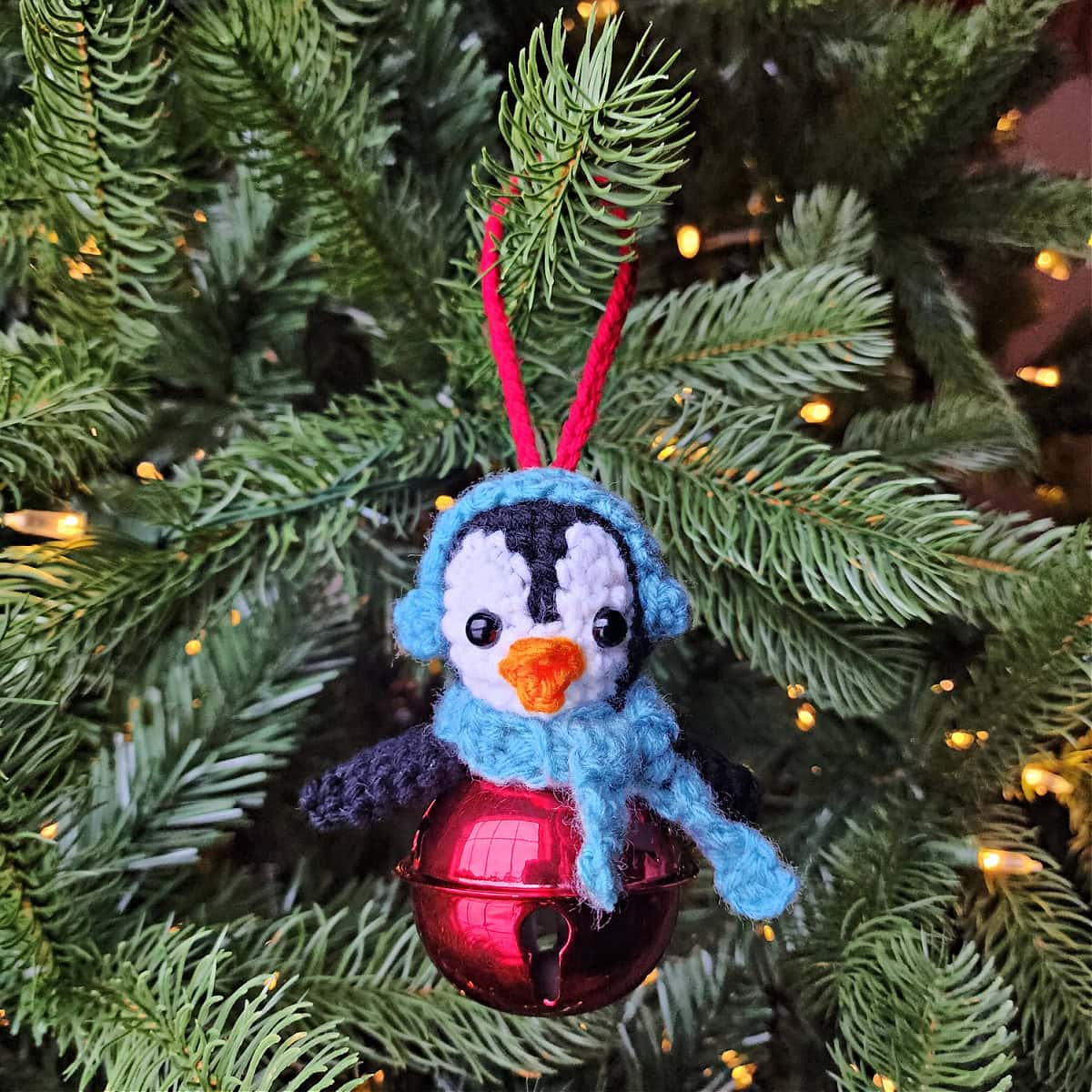 Cute crochet penguin jingle bell ornament with blue earmuffs and scarf.