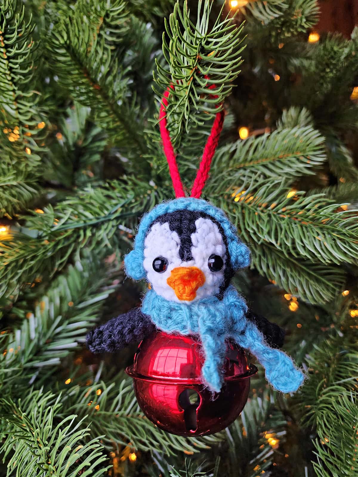 Crochet penguin jingle bell ornament hanging on a Christmas tree.