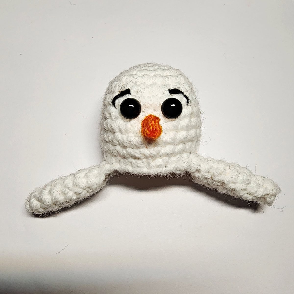 Crochet snowman head and arms with nose, eyes, and eyebrows.