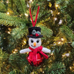 Crochet snowman jingle bell ornament hanging on a Christmas tree.