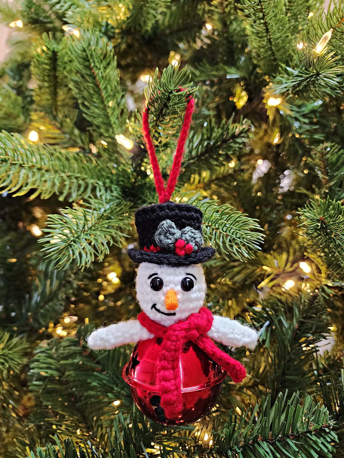 Crochet snowman jingle bell ornament hanging on a pre-lit Christmas tree.