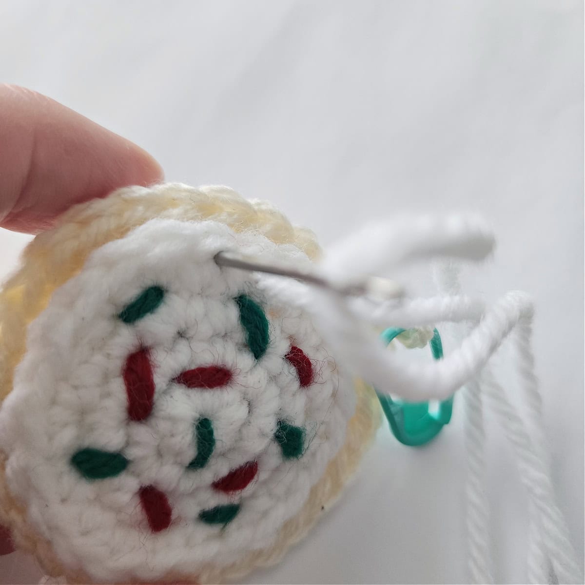 Close-up of the frosting being sewn onto a crochet sugar cookie ornament.