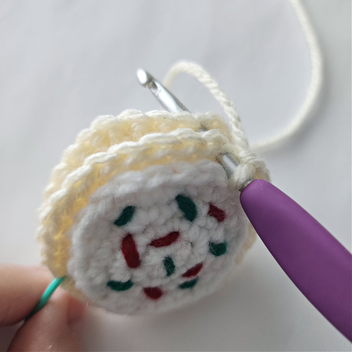 A purple crochet hook slip stitching the two cookies together to make a sugar cookie.