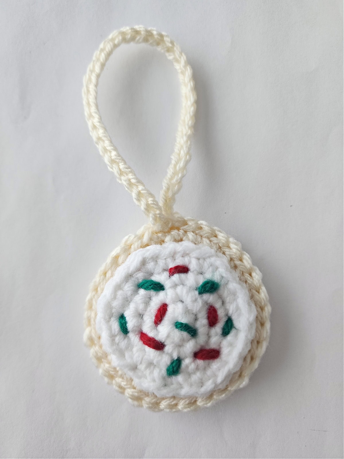 Crochet sugar cookie Christmas ornament with white frosting and red and green sprinkles.