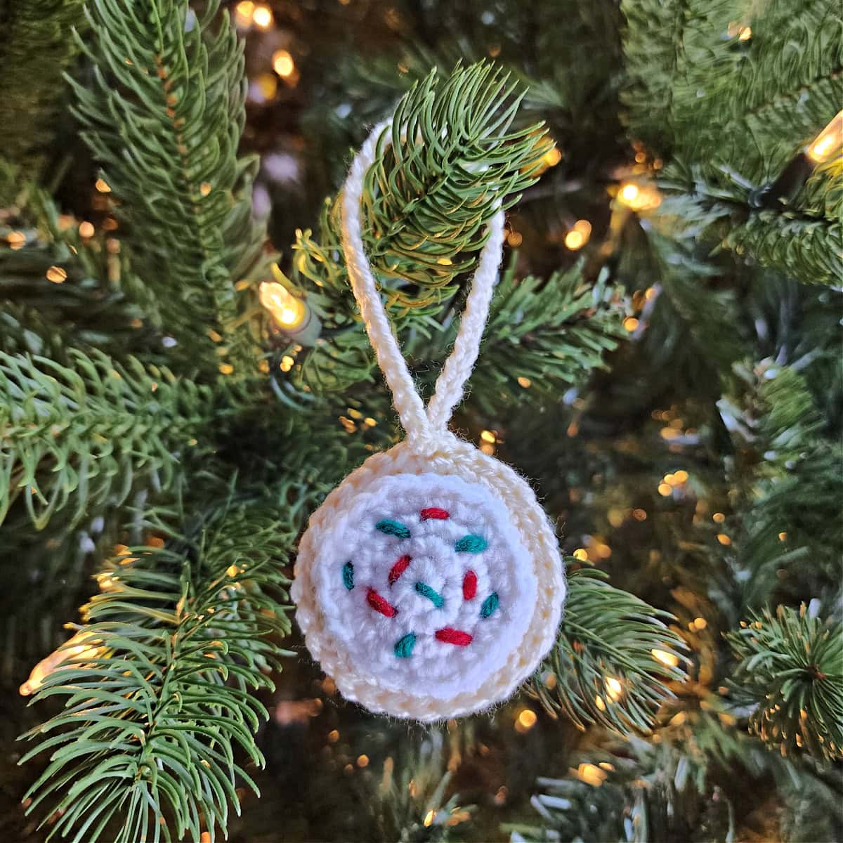 Crochet sugar cookie ornament with red and green sprinkles hanging on a Christmas tree.