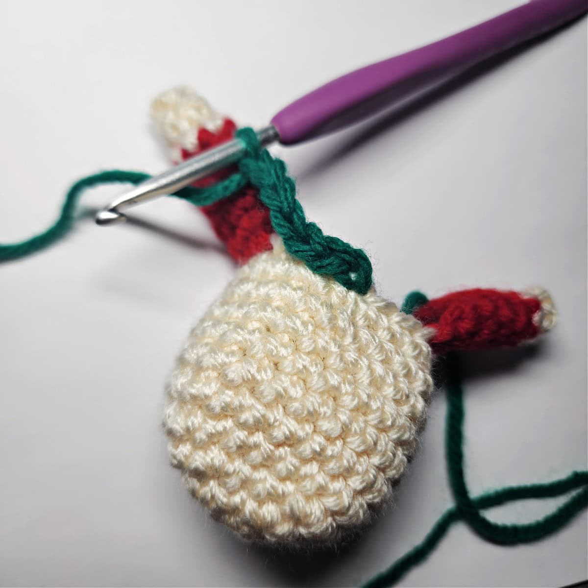 Green yarn attached to the elf's head with a purple crochet hook.