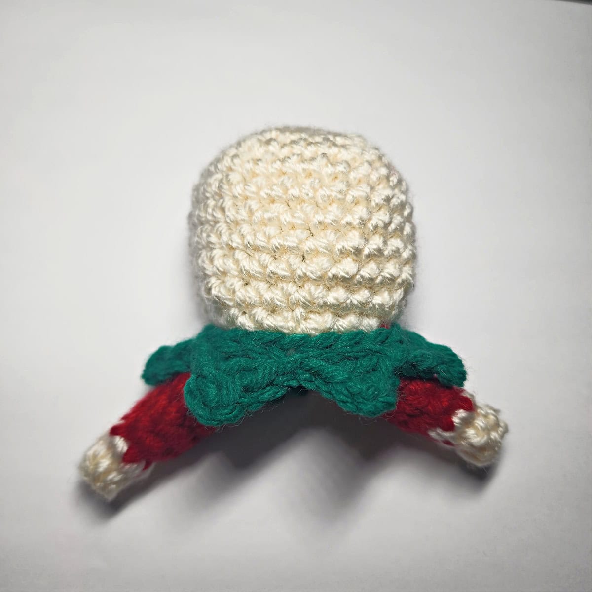 A small ivory crochet head with a green pointed collar and red arms.