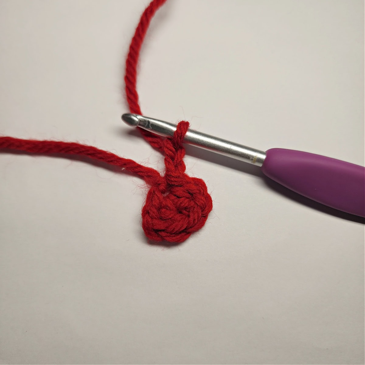 A small red yarn circle with a chain attached to become a mini crochet bow.