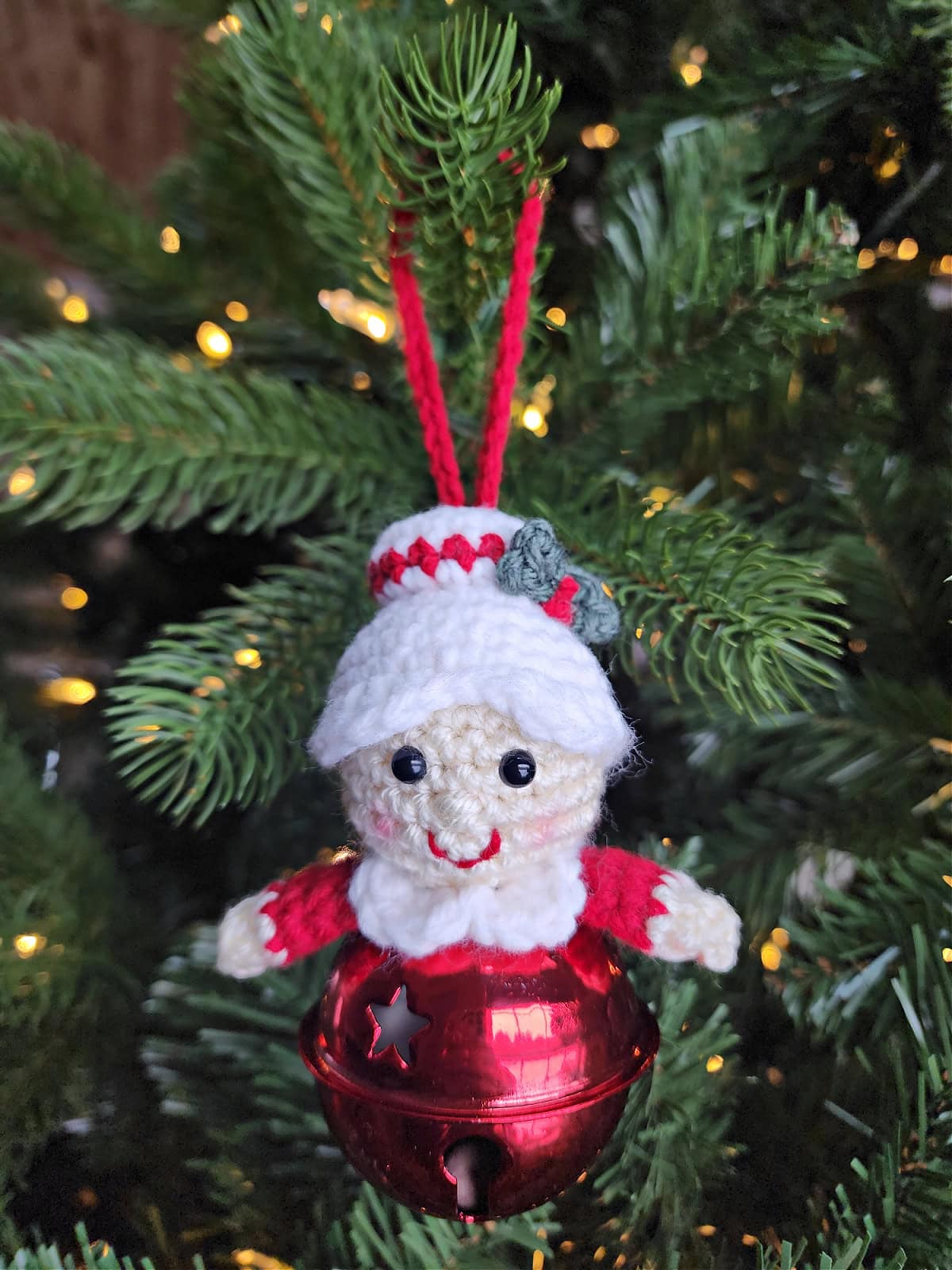 Mrs Claus crochet jingle bell ornament hanging on a Christmas tree.