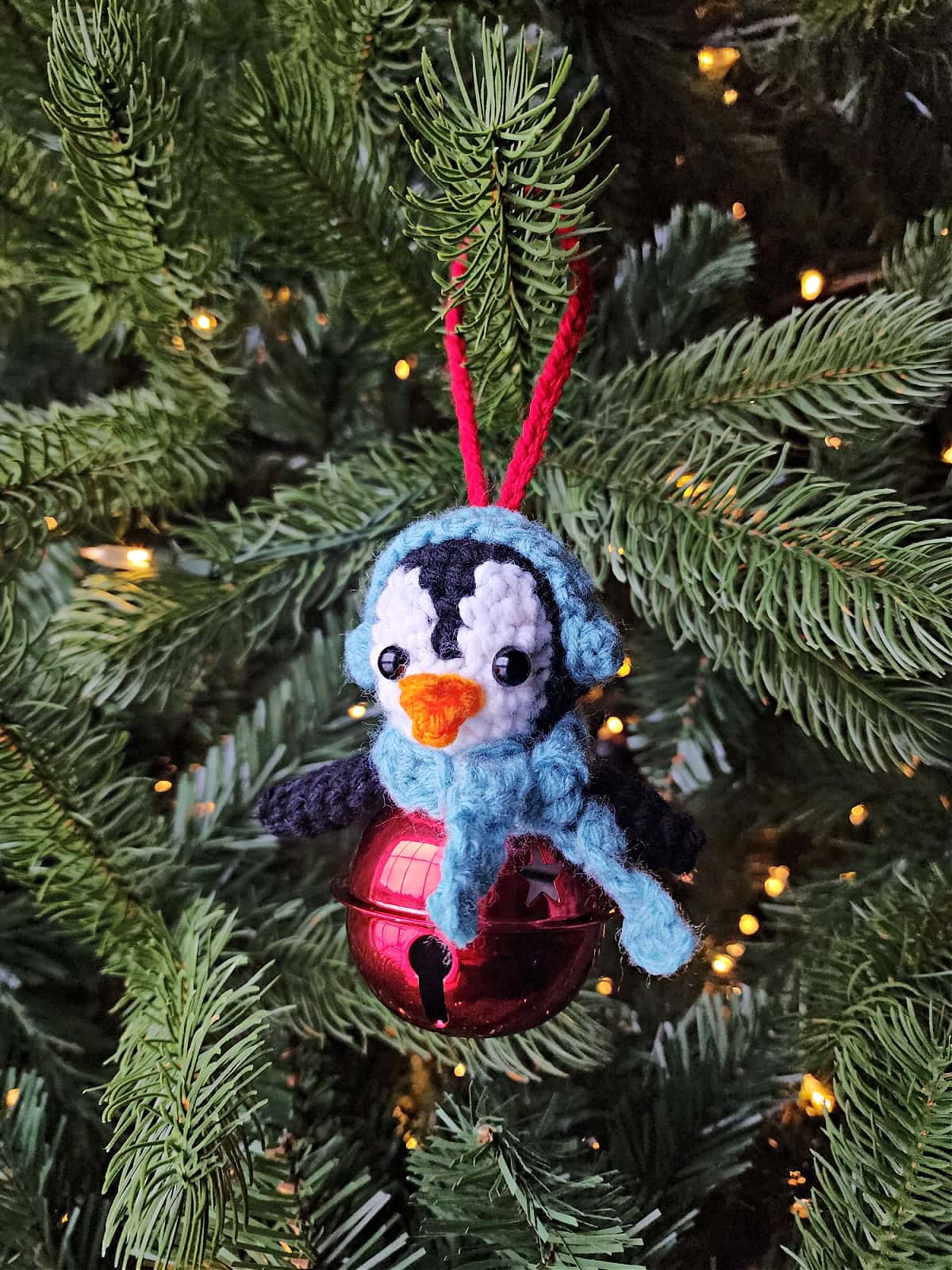 Crochet penguin hanging on a pre-lit Christmas tree.