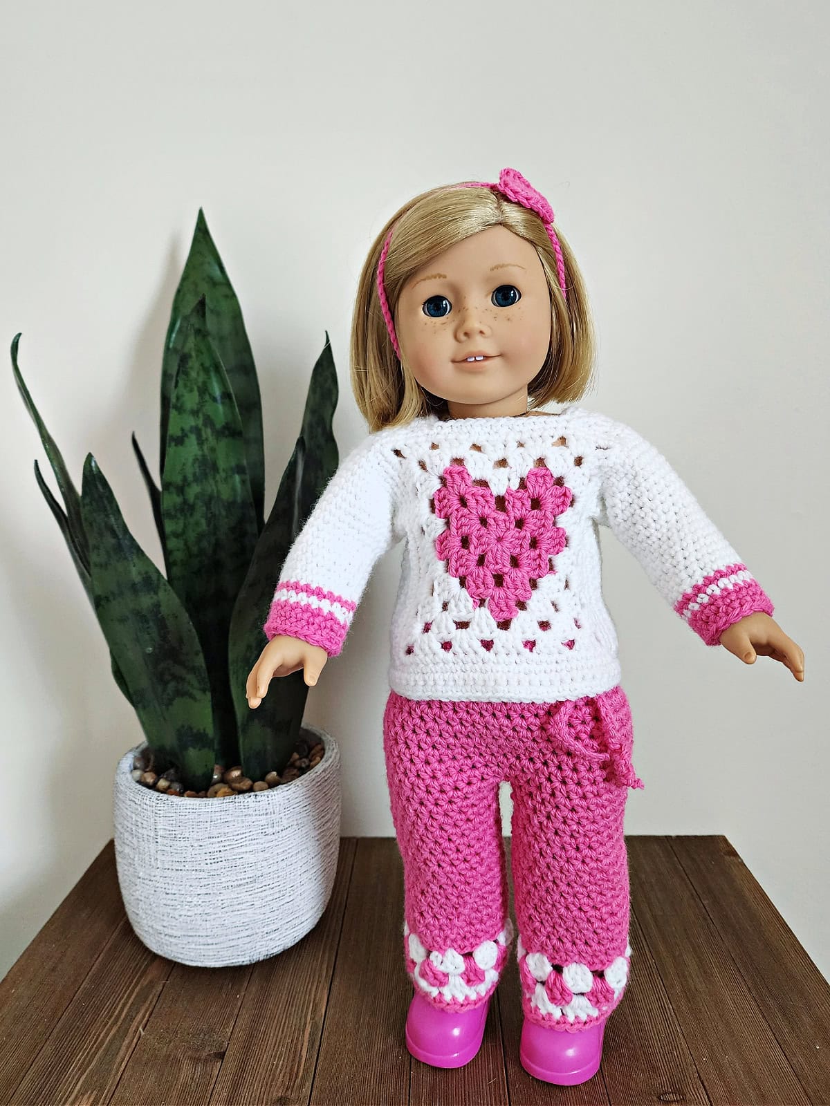 18" doll wearing crochet doll clothes and pink shoes and standing by a potted plant.