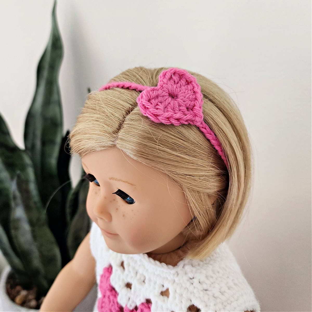 A small pink crochet heart headband being worn by an 18 inch doll.