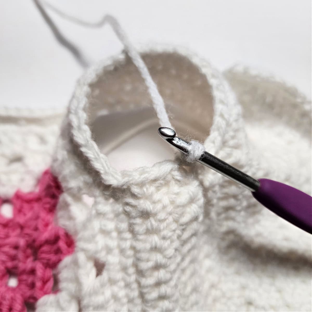 The purple crochet hook is showing where to join the yarn to crochet sleeves on the crochet doll sweater.