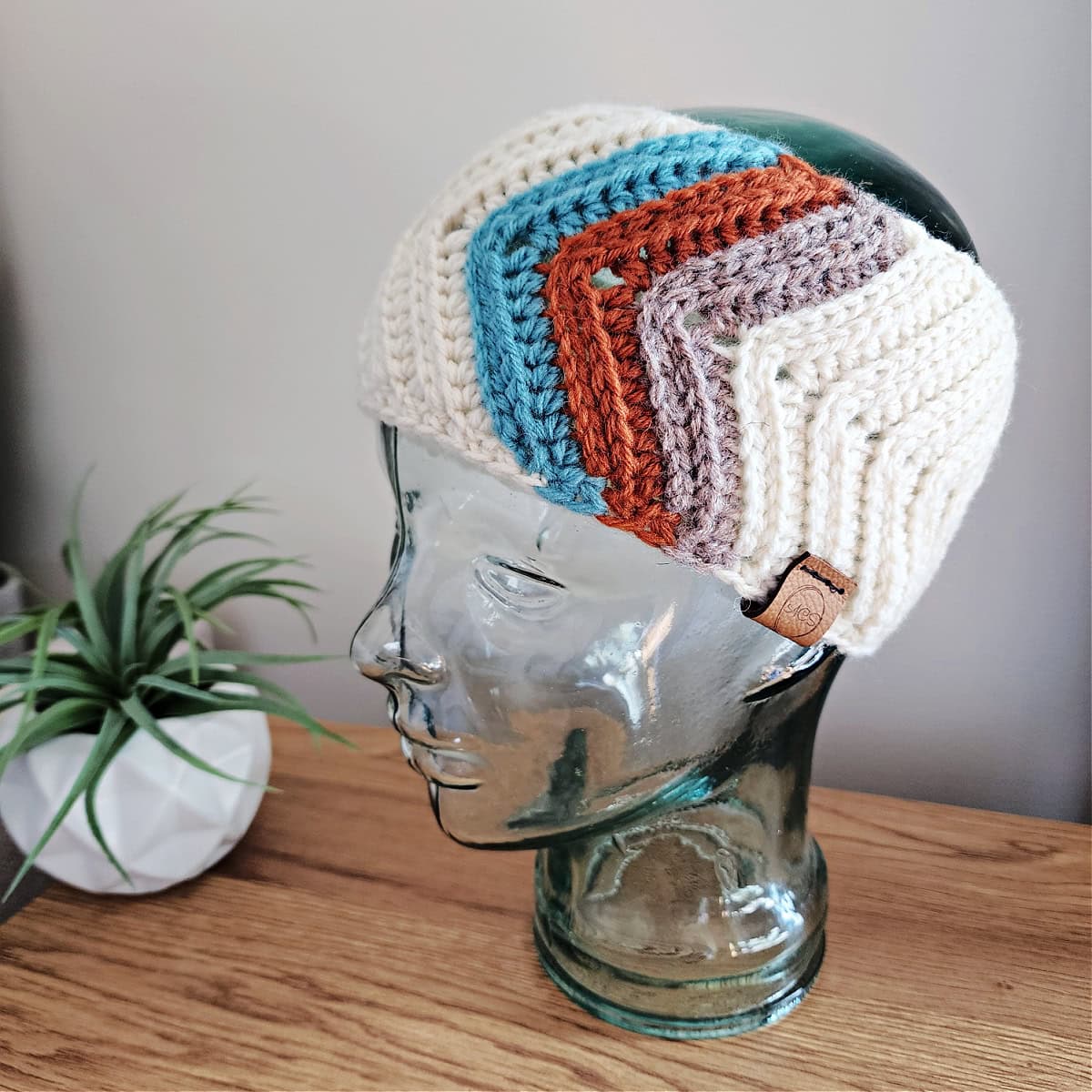 Crochet ear warmer with retro stripes on a glass mannequin head.