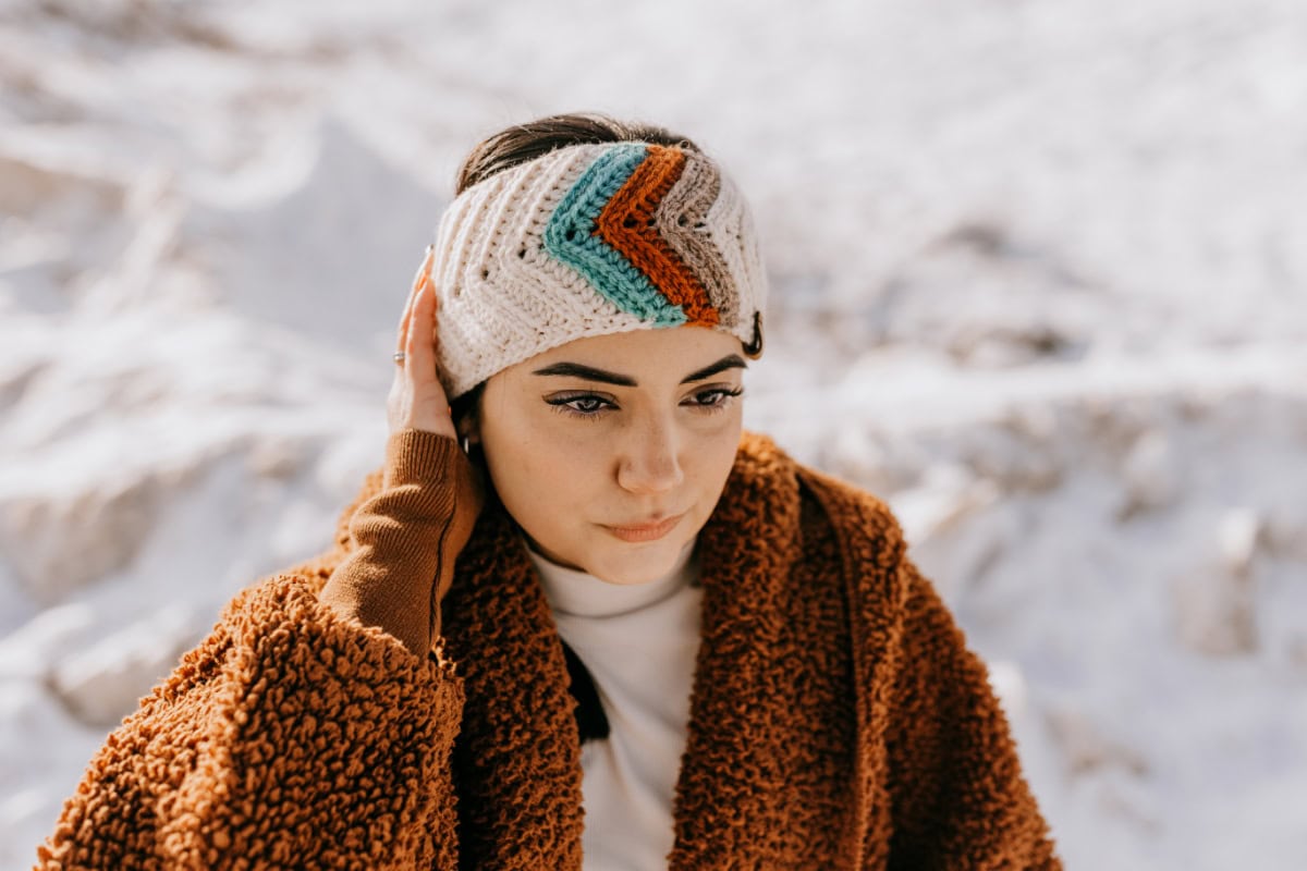 Crochet ear warmer with retro stripes modeled by a woman wearing a fuzzy jacket.