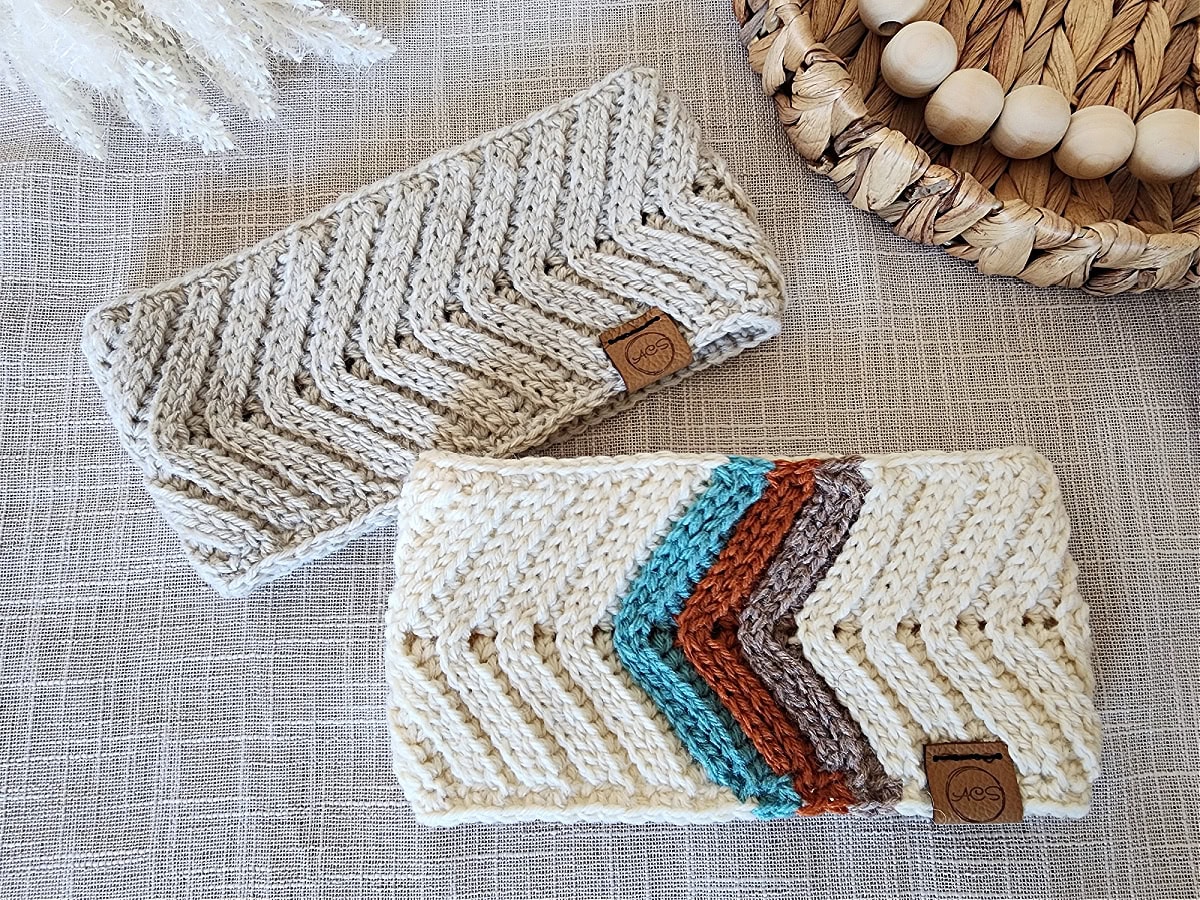 Two crochet ear warmers laying on a light taupe linen fabric with a wooden tray and beads.