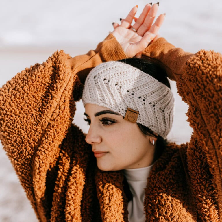 Crochet ear warmer modeled by a woman wearing a rust colored winter jacket.