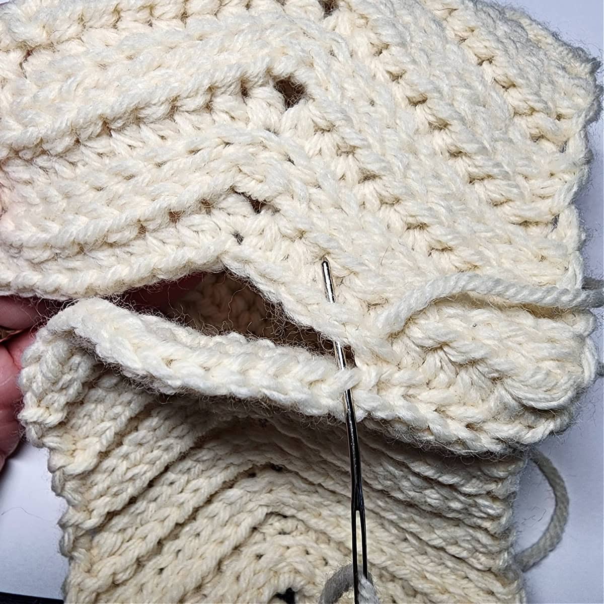 A metal yarn needle showing which loops to whipstitch together to seam the knit-look crochet ear warmer.