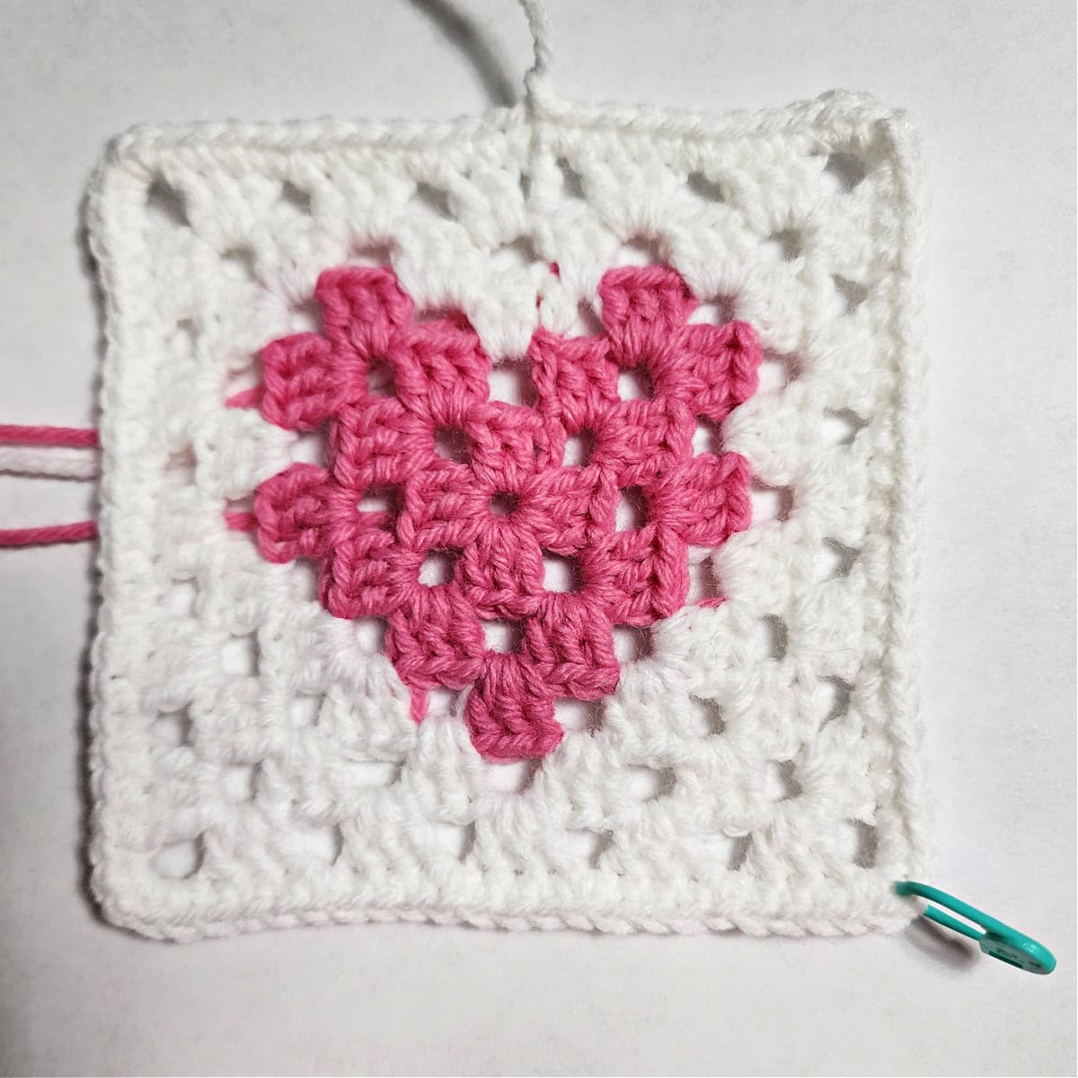 A crochet heart granny square complete with a green stitch marker to mark a stitch for later.